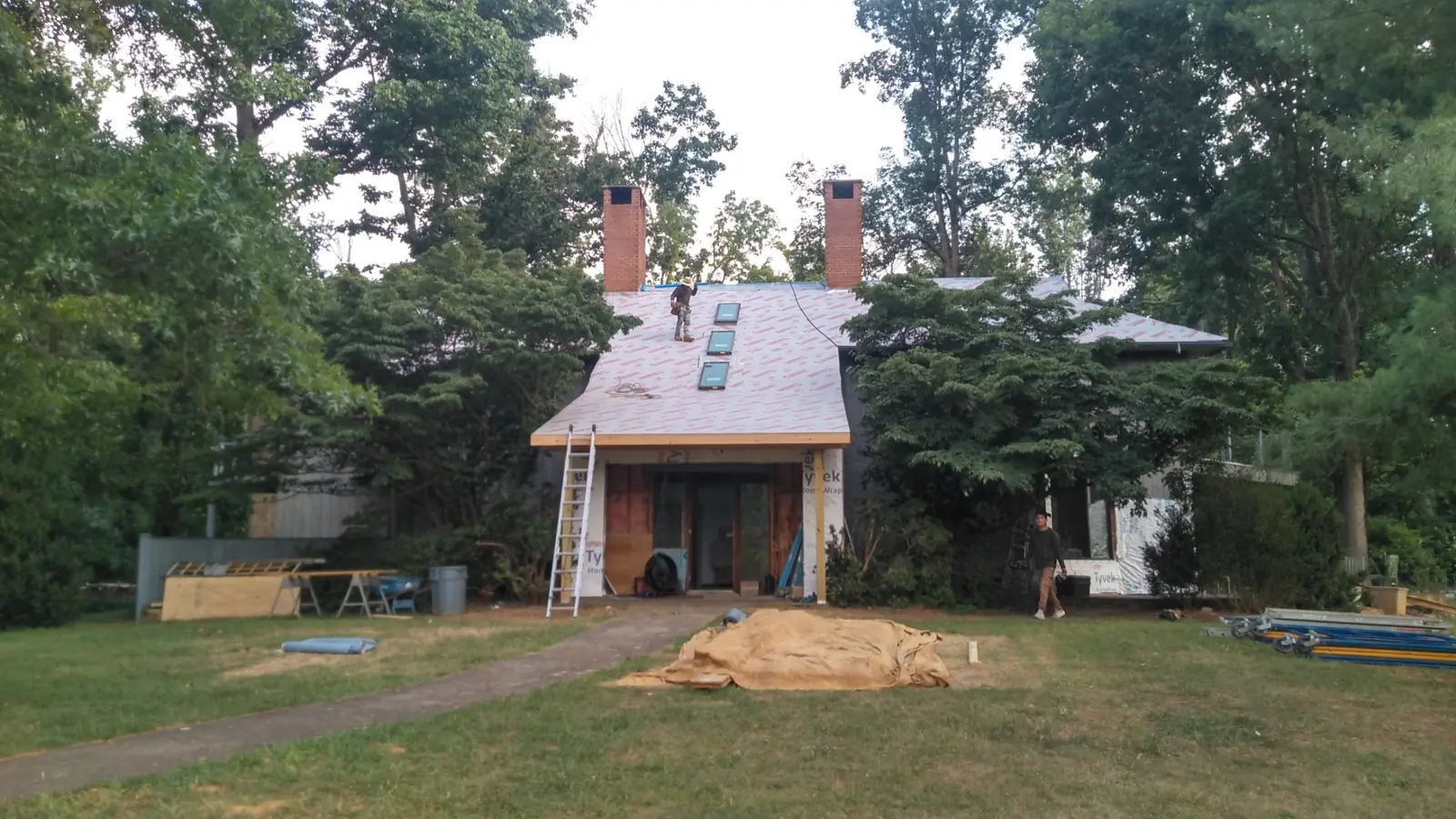 House set among trees with the roof under underlayment and a ladder at the eave.