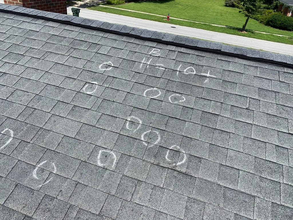 Grey roof shingles with chalk circles marking spots of concern during a roof inspection.