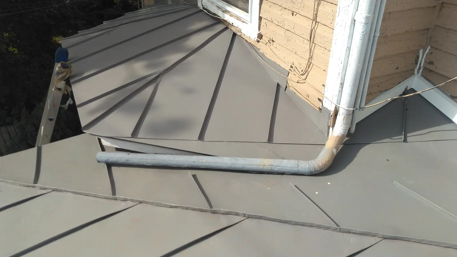 Slate gray metal porch roof around a downspout and white trim.