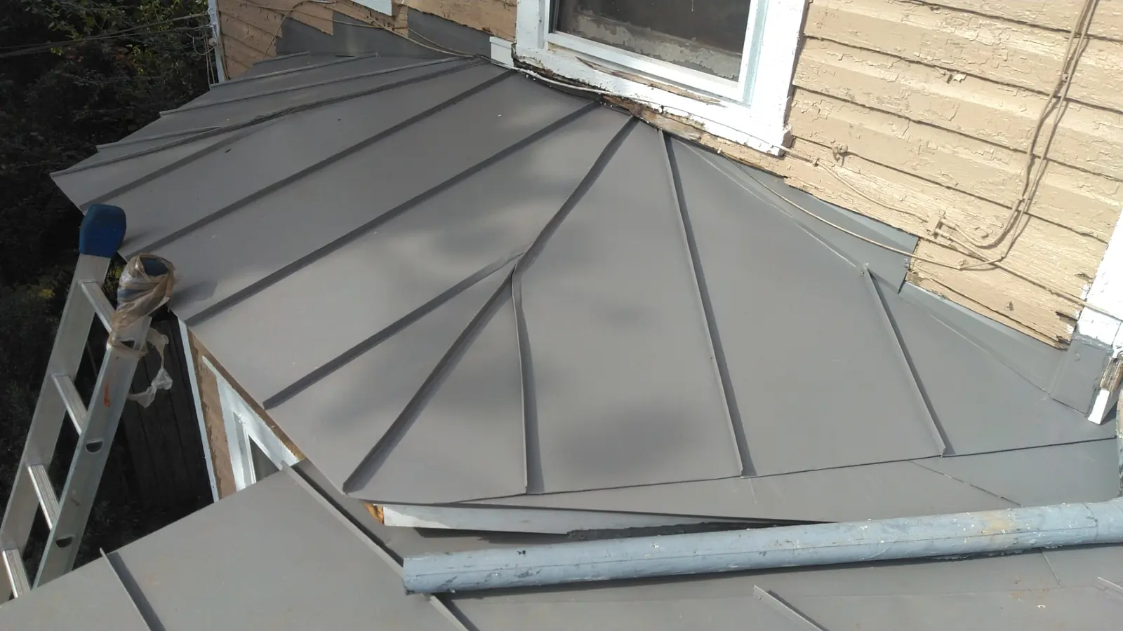 Slate gray metal roof at a wall corner with a ladder against the siding.