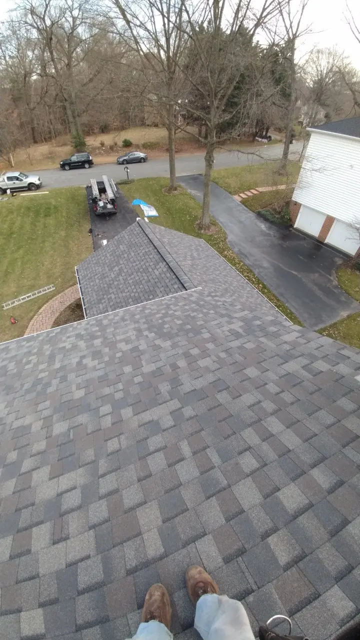 Shingle courses and rake edge on a gray-brown roof with a driveway below.