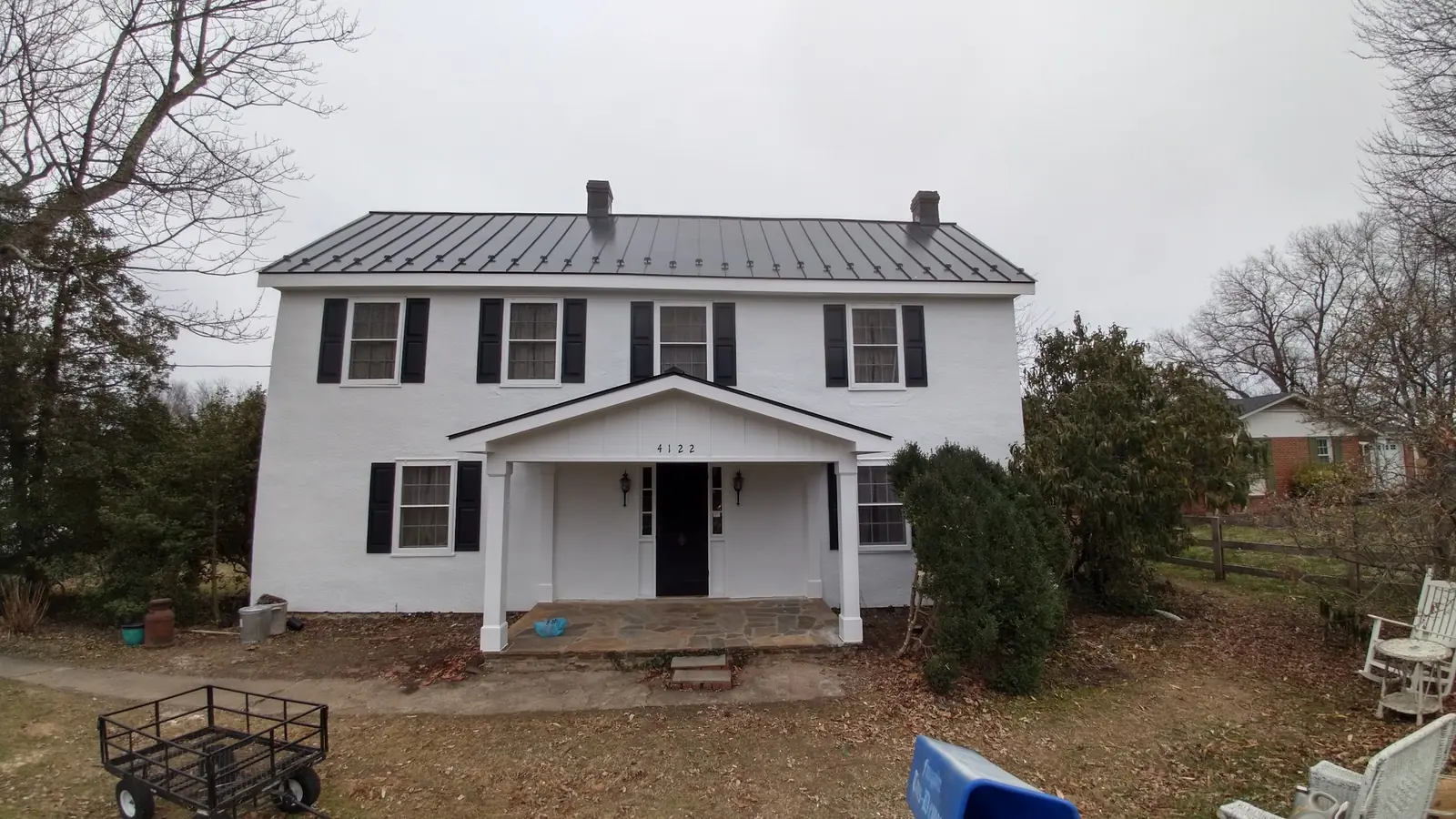 Front of the white colonial with the dark metal roof and a trailer in the foreground.