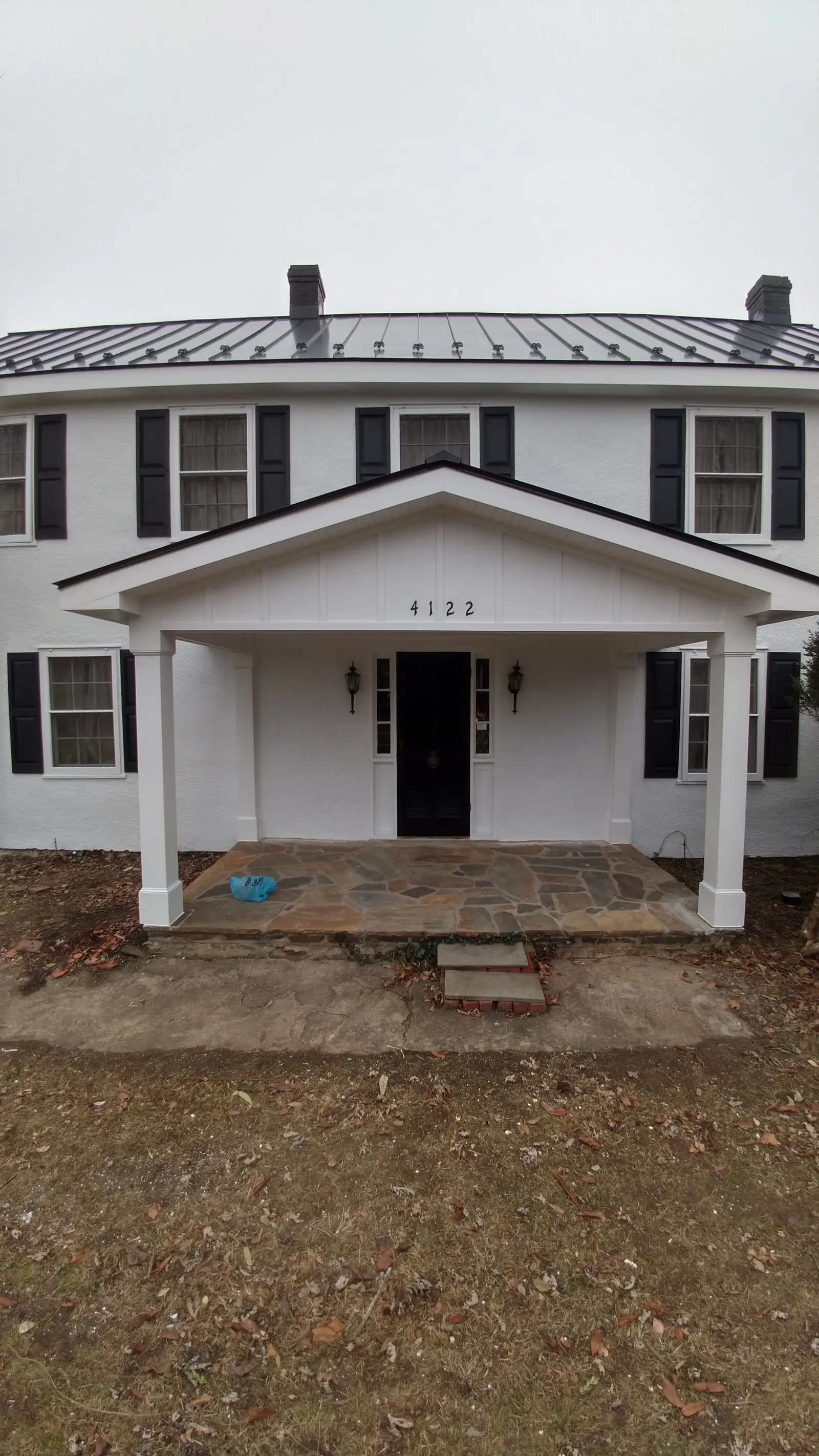 White colonial front porch with a dark metal roof above and a stone walk.