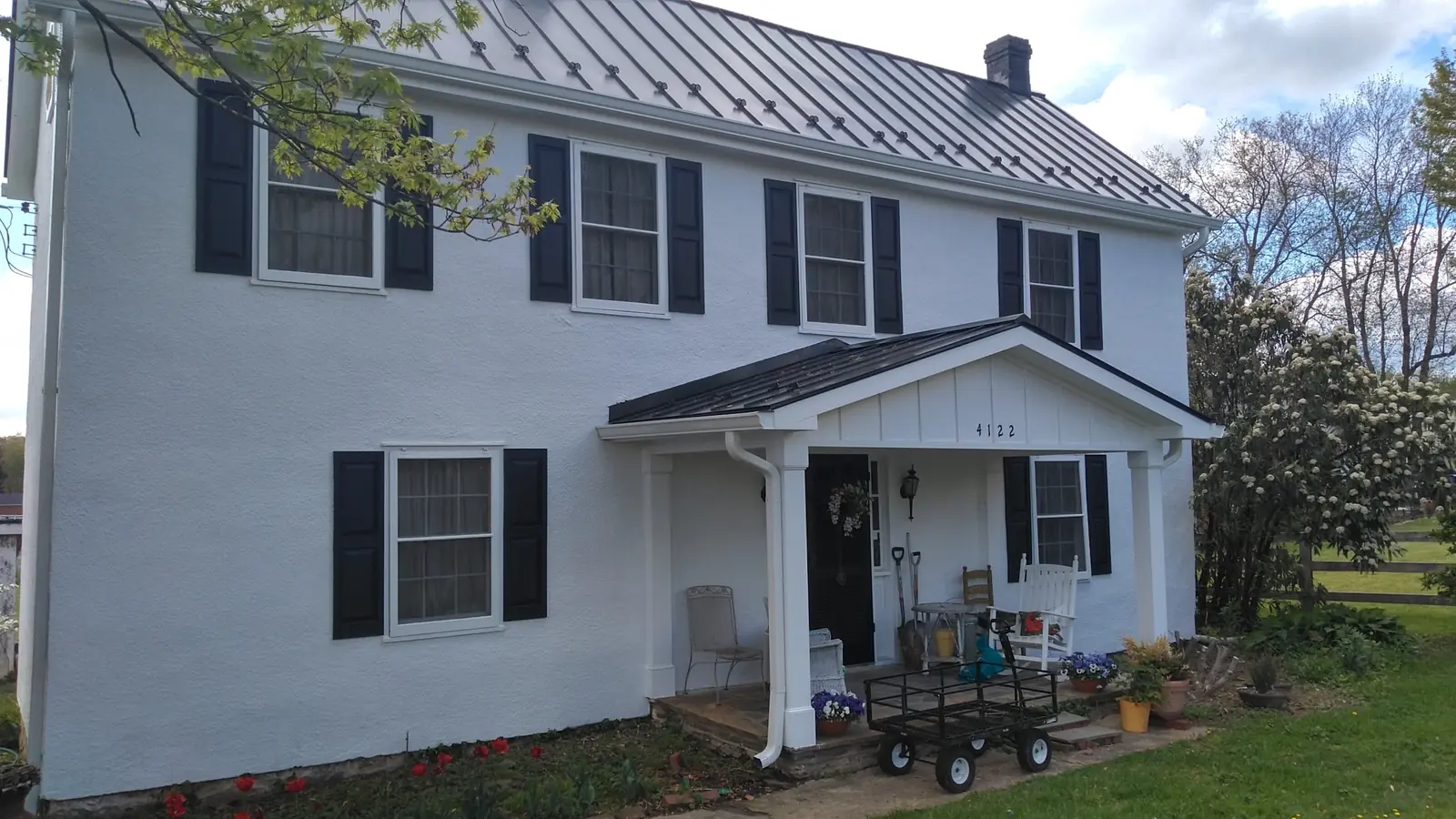 White colonial with a dark metal roof and a front porch with columns.