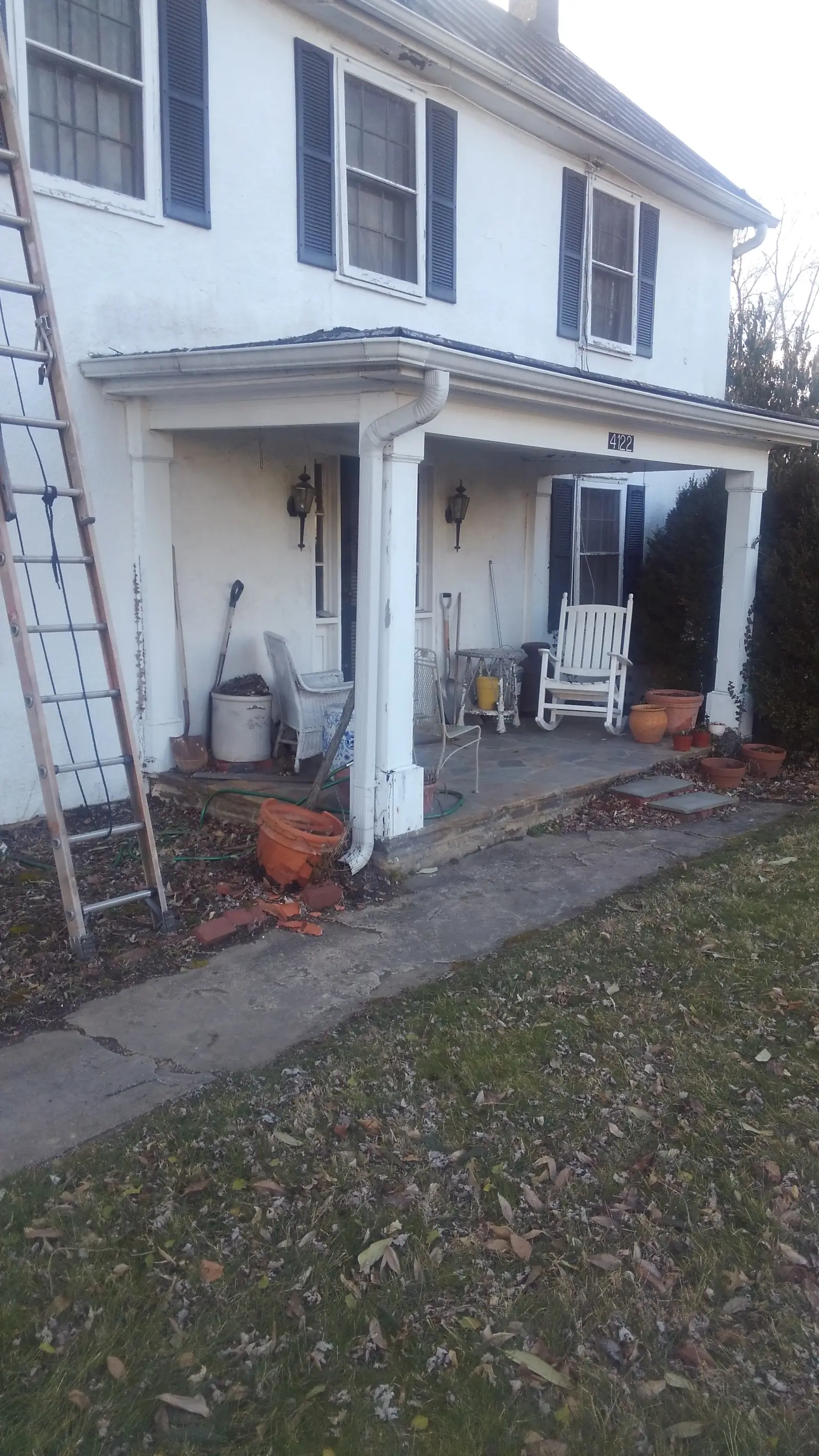 Front porch of the white colonial with a ladder against the column.