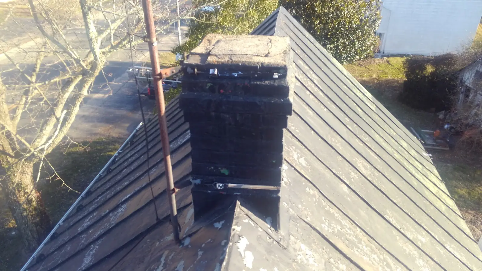 Gray roof with a blackened chimney seen from the roof.