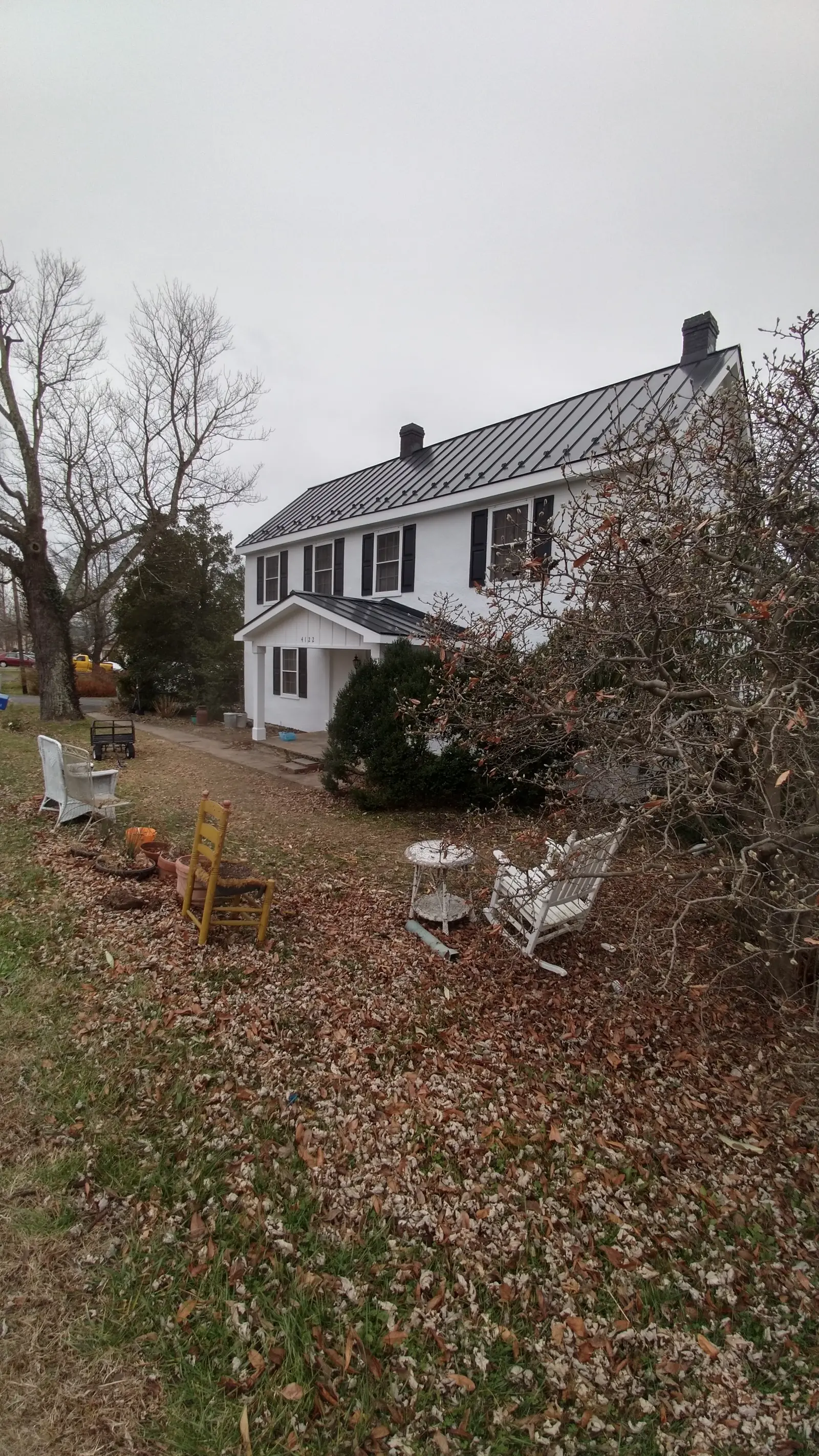 White colonial and its yard with a dark metal roof seen at a distance.