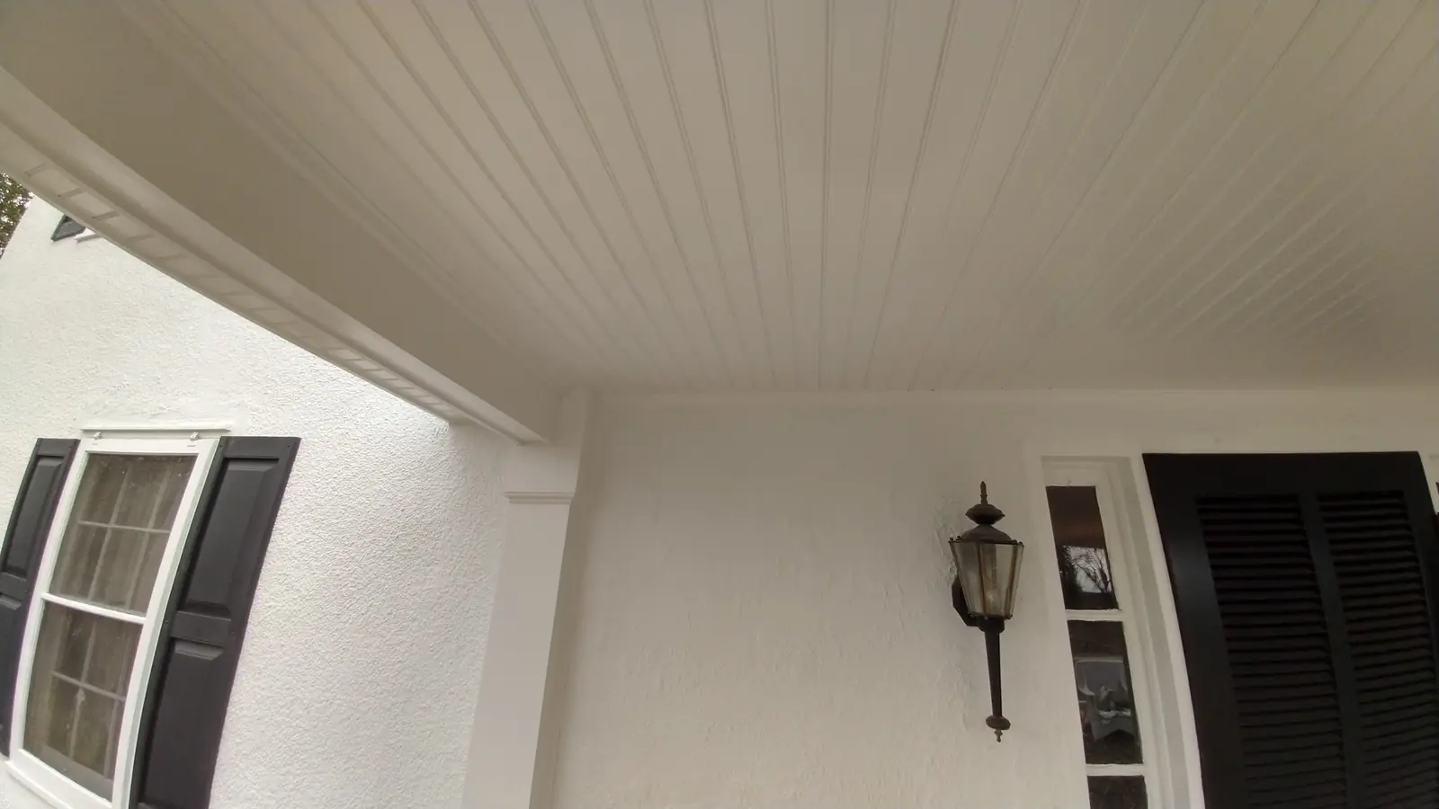 White painted porch ceiling and trim beside black shutters and a lantern.