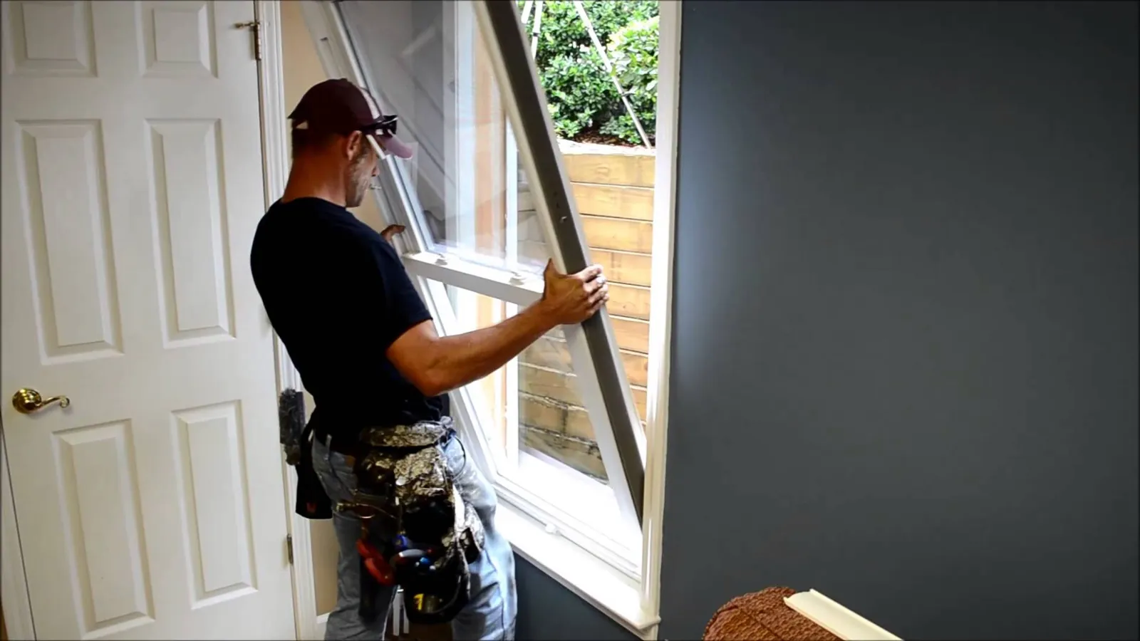 Installer carefully lifting a replacement window into an interior opening.